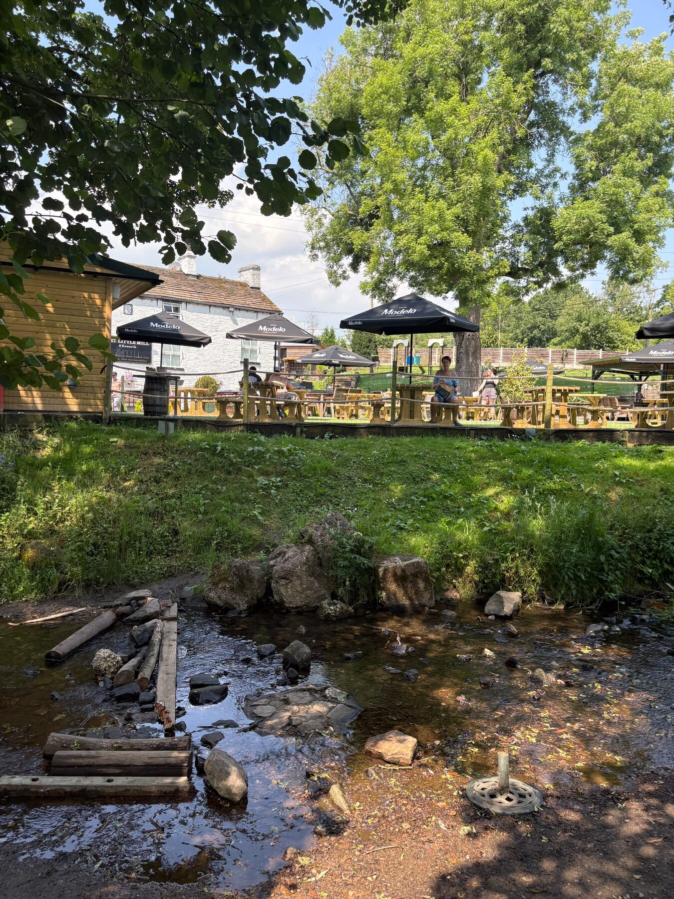 Rowarth Brook running past the beer garden and parasols in the grounds of The Little Mill Inn