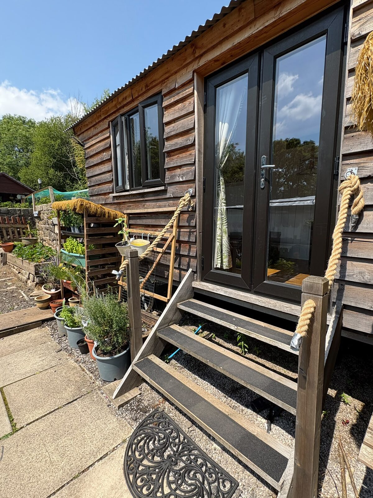 Timber-clad shepherd's hut with black French doors and timber steps up from the garden