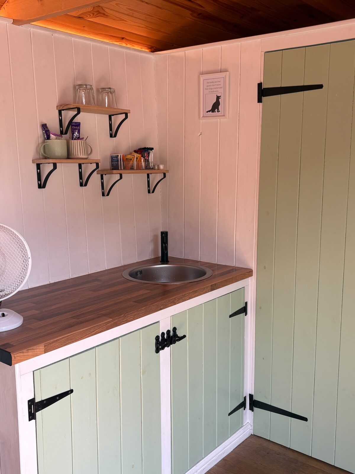 Compact kitchenette with sage-green units and a sink inside the shepherd's hut