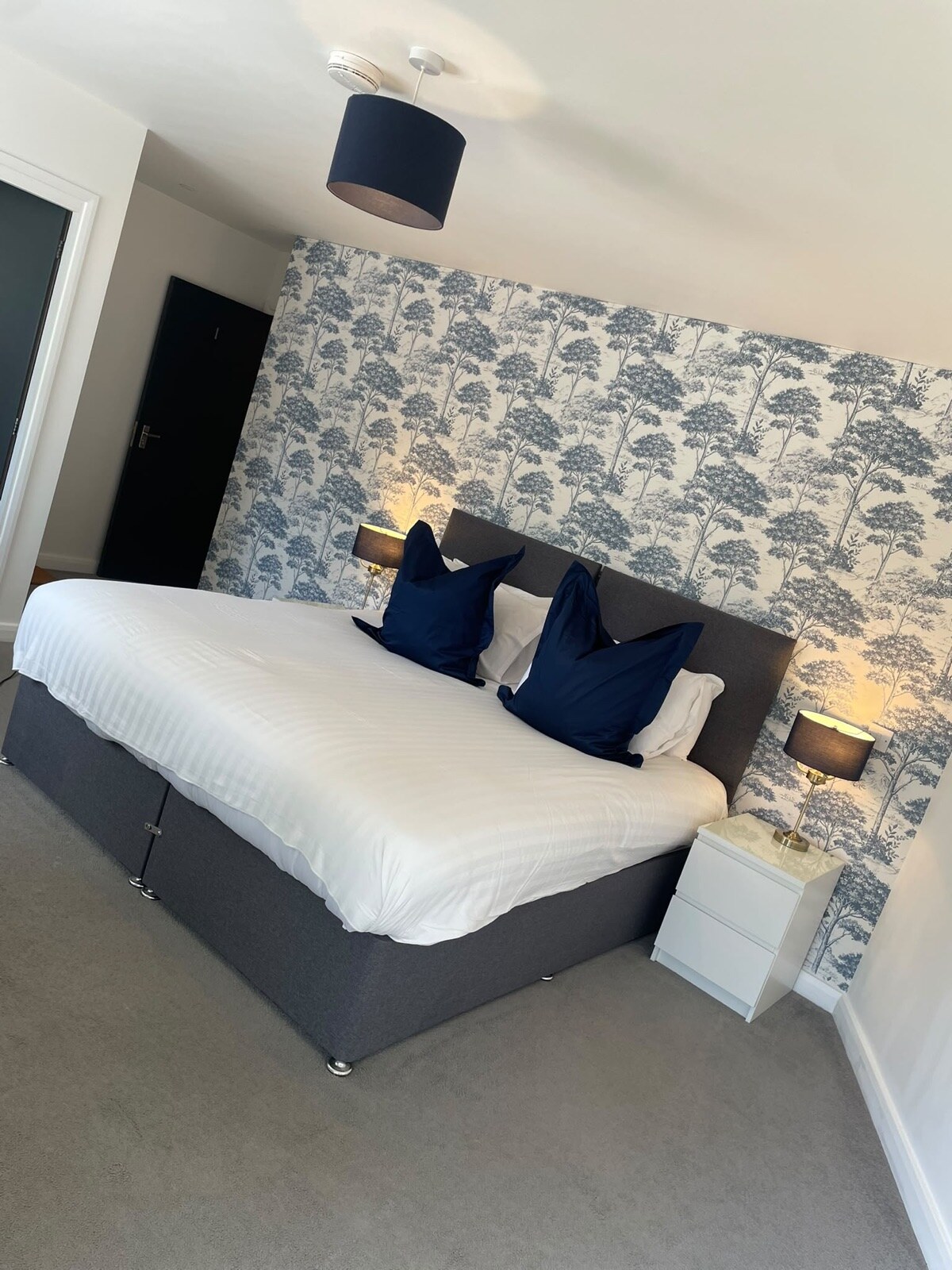 Freshly styled double bed with navy cushions against botanical feature wallpaper