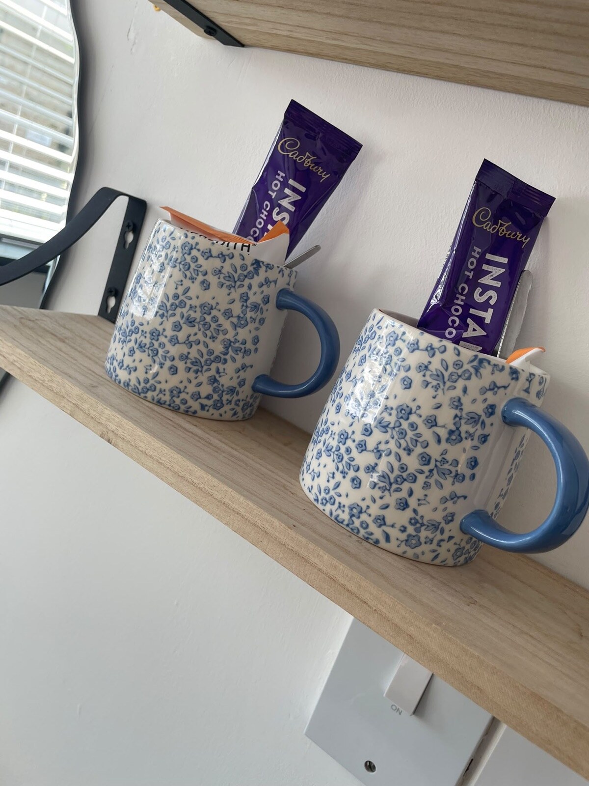 In-room welcome tray with mugs and hot chocolate on a wooden shelf